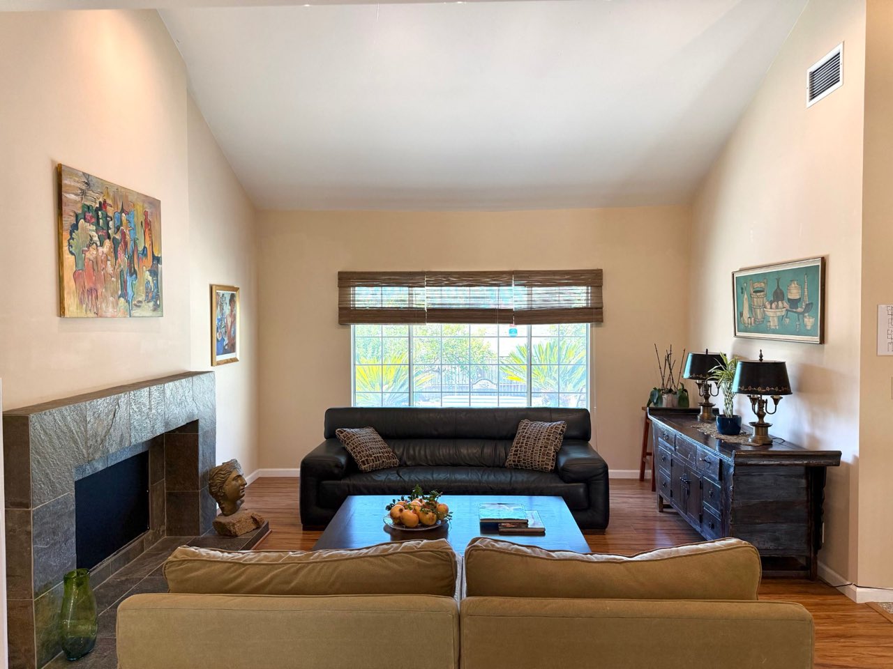 A bright living room with a high ceiling, two sofas, a fireplace and a window onto the garden